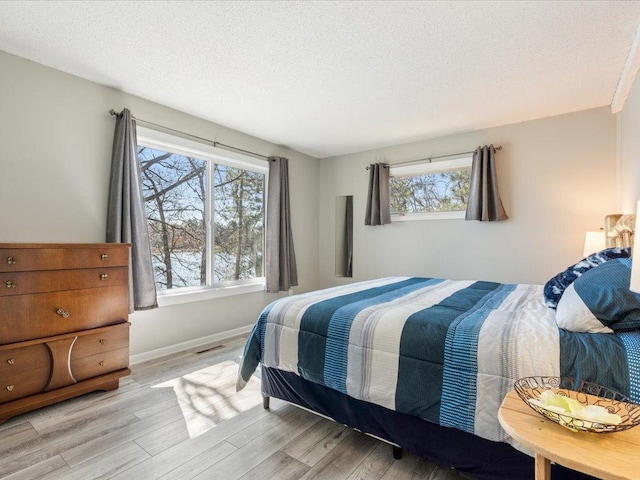 bedroom featuring baseboards, light wood finished floors, a textured ceiling, and visible vents