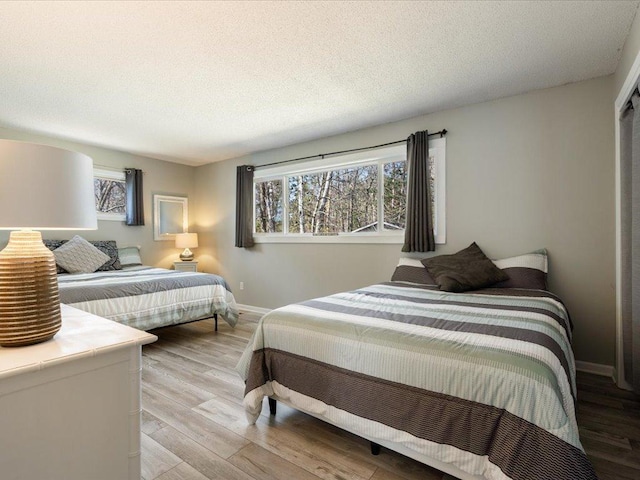 bedroom with baseboards, a textured ceiling, and wood finished floors