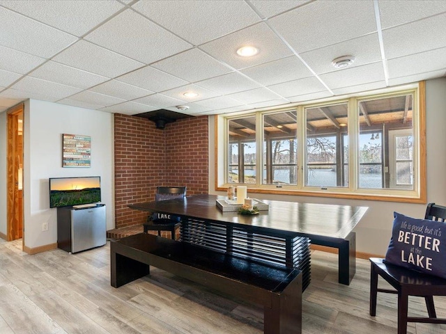 dining area with baseboards, light wood-style flooring, and a drop ceiling