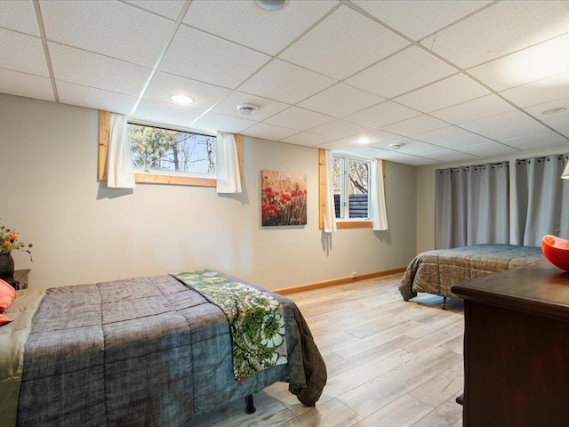 bedroom featuring baseboards, light wood finished floors, and a drop ceiling
