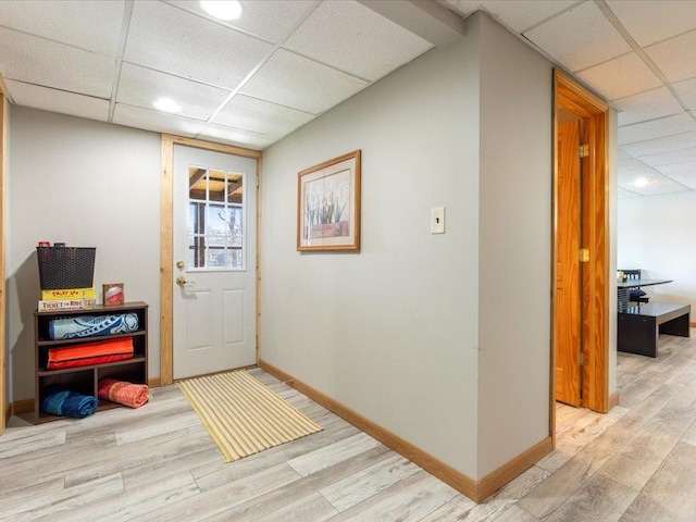 doorway to outside with baseboards, a paneled ceiling, and light wood finished floors