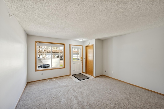carpeted foyer with a textured ceiling and baseboards
