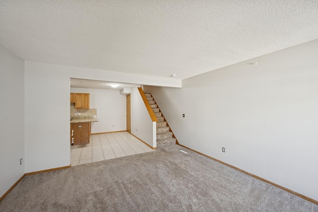 unfurnished living room with light colored carpet, a textured ceiling, baseboards, and stairs