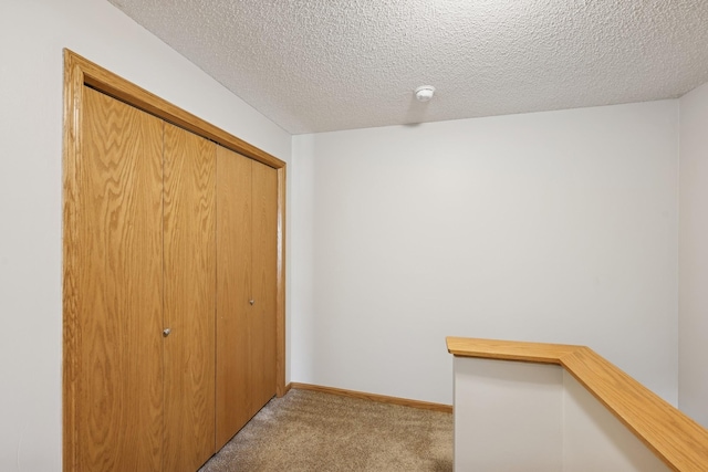 hall with carpet floors, a textured ceiling, and baseboards