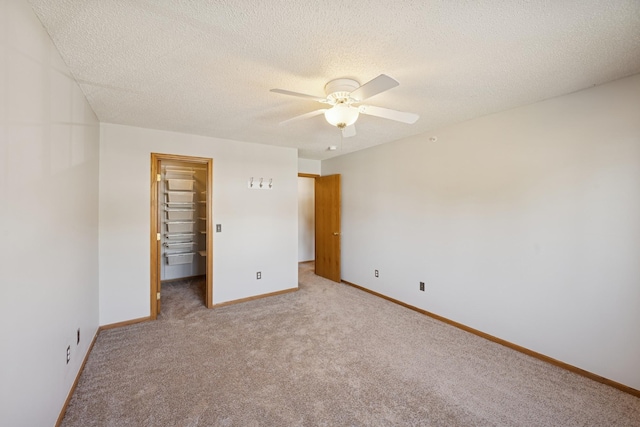 unfurnished bedroom featuring a walk in closet, ceiling fan, a textured ceiling, baseboards, and carpet