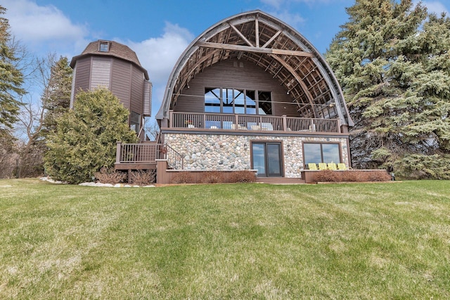 rear view of property featuring a lawn, a balcony, and stone siding
