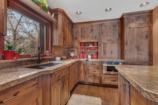 kitchen featuring light stone countertops, brown cabinets, a sink, wood-type flooring, and stainless steel oven