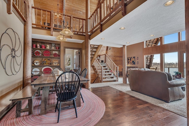 dining area featuring wooden walls, hardwood / wood-style flooring, stairs, and a towering ceiling