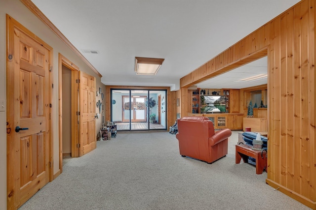living room with ornamental molding, visible vents, wood walls, and carpet floors
