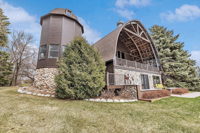 rear view of property with a lawn, stone siding, a shingled roof, and a balcony