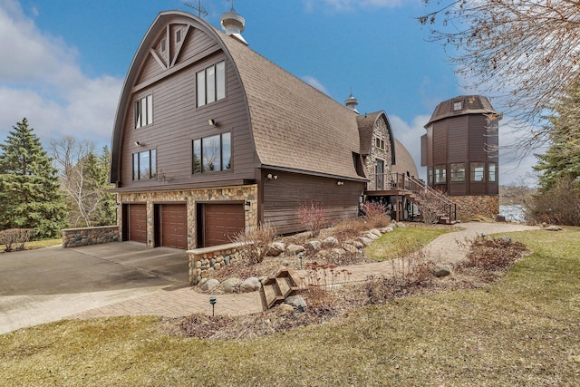 view of side of home with stone siding, roof with shingles, stairway, a gambrel roof, and a garage