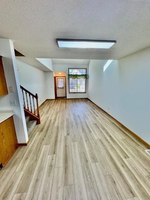 unfurnished living room with light wood-style flooring, a textured ceiling, stairway, and baseboards