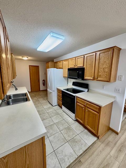 kitchen with electric range oven, black microwave, a sink, freestanding refrigerator, and a textured ceiling