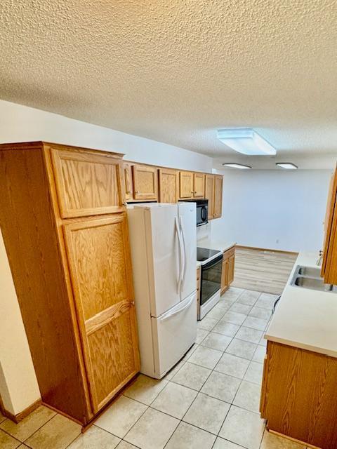 kitchen with freestanding refrigerator, electric range oven, a sink, light tile patterned floors, and brown cabinets