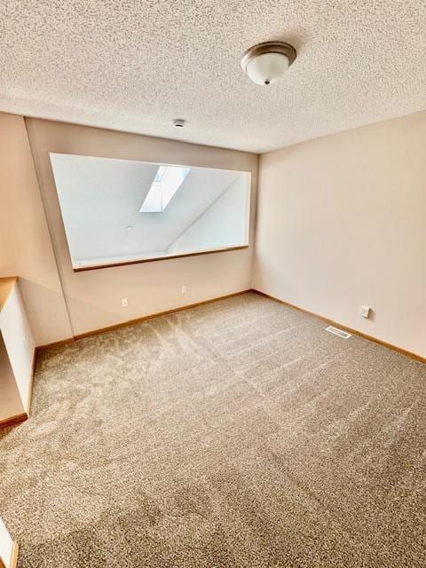 unfurnished room with a skylight, baseboards, a textured ceiling, and carpet