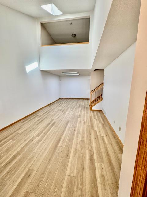 unfurnished living room with a skylight, wood finished floors, baseboards, and stairway