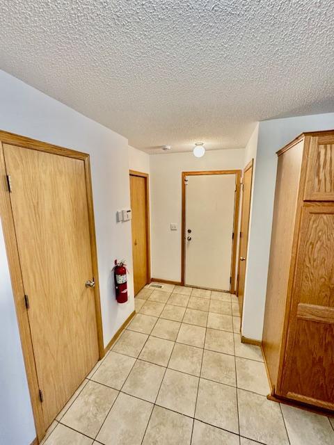 corridor with light tile patterned floors, baseboards, and a textured ceiling