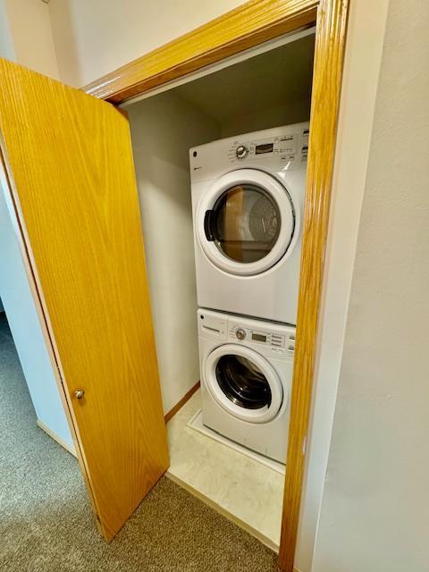 clothes washing area featuring stacked washer and clothes dryer and carpet
