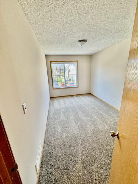 carpeted empty room featuring a textured ceiling and baseboards