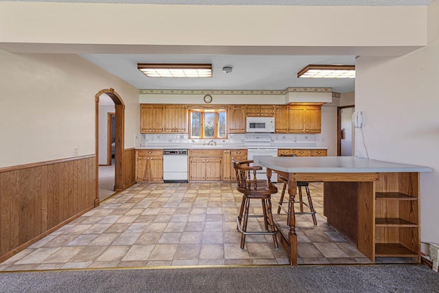 kitchen featuring a sink, white appliances, stone finish floor, light countertops, and wainscoting