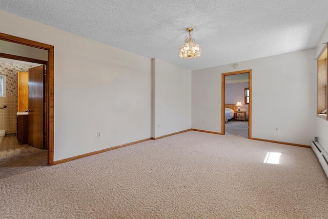 carpeted empty room with an inviting chandelier, a textured ceiling, and baseboards