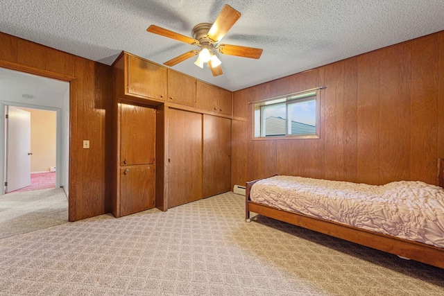 bedroom featuring light carpet, a closet, wooden walls, and a ceiling fan