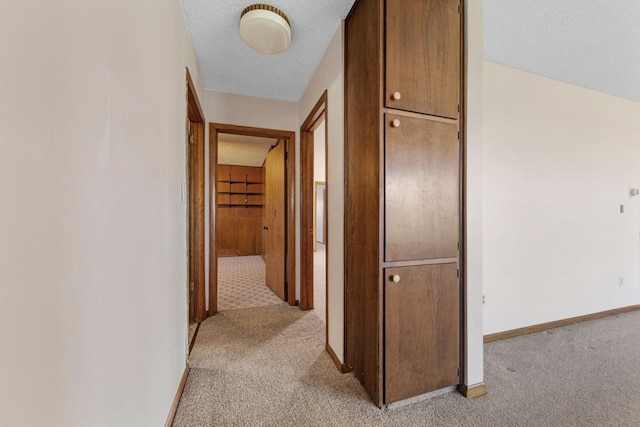 corridor with a textured ceiling, light carpet, and baseboards