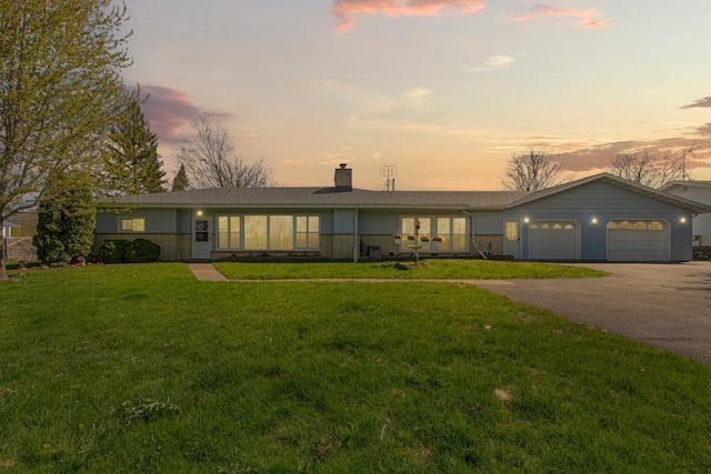 ranch-style house featuring driveway, a chimney, a front yard, an attached garage, and brick siding