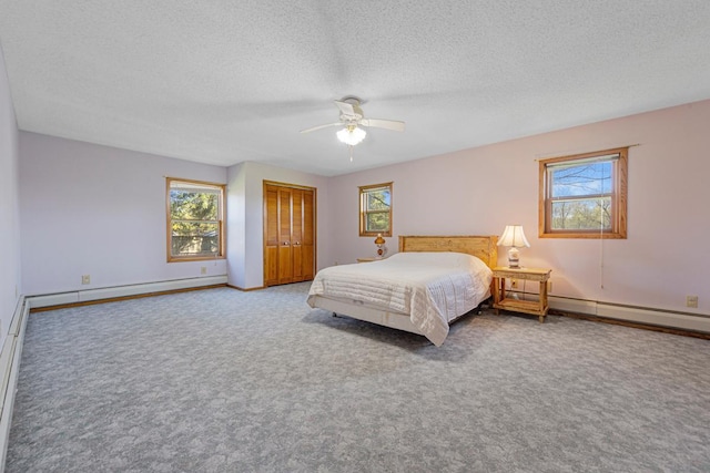 carpeted bedroom with multiple windows, a textured ceiling, a closet, and a baseboard radiator