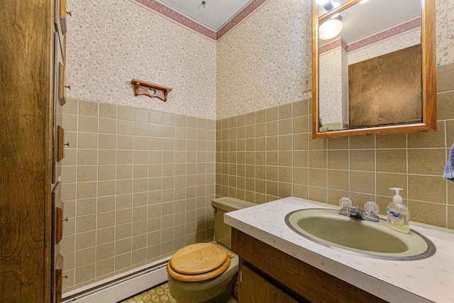 bathroom featuring toilet, wallpapered walls, a baseboard radiator, tile walls, and vanity
