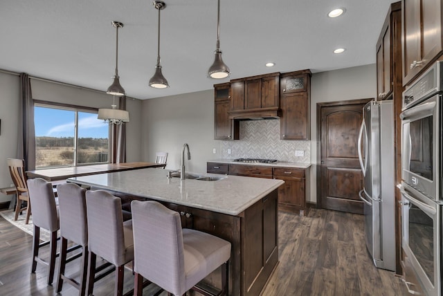 kitchen featuring dark wood-style flooring, dark brown cabinets, a sink, stainless steel appliances, and decorative backsplash