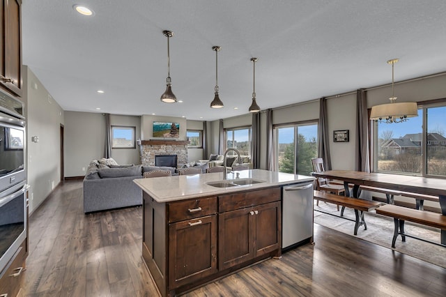 kitchen featuring a stone fireplace, appliances with stainless steel finishes, dark brown cabinets, a sink, and dark wood-style floors