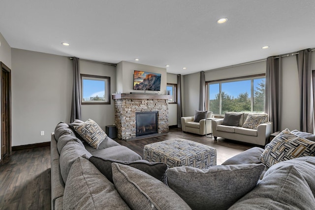 living room with dark wood-style flooring, baseboards, a stone fireplace, and a healthy amount of sunlight