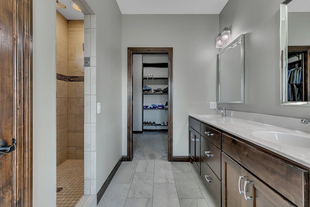 full bathroom with double vanity, a walk in closet, a tile shower, and a sink