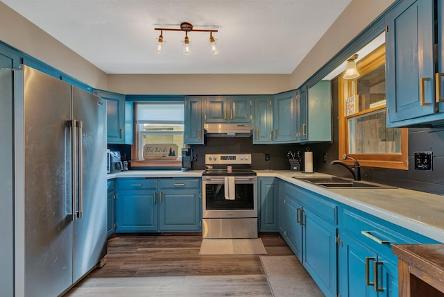 kitchen featuring a sink, stainless steel appliances, light countertops, dark wood finished floors, and under cabinet range hood