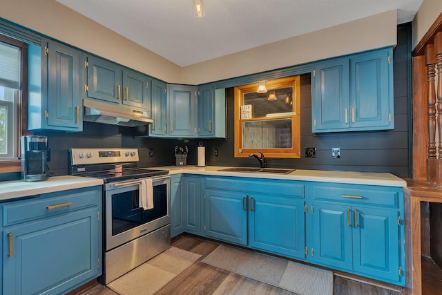 kitchen with under cabinet range hood, light countertops, electric stove, a sink, and dark wood-type flooring