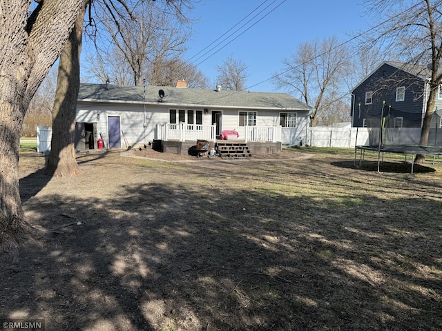 rear view of property with a trampoline, a chimney, fence, and a deck