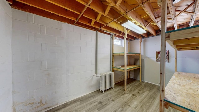 basement with radiator, wood finished floors, and concrete block wall