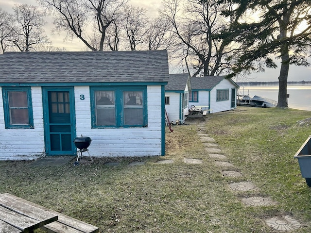 view of front of house featuring a front lawn, a water view, an outbuilding, and a shingled roof