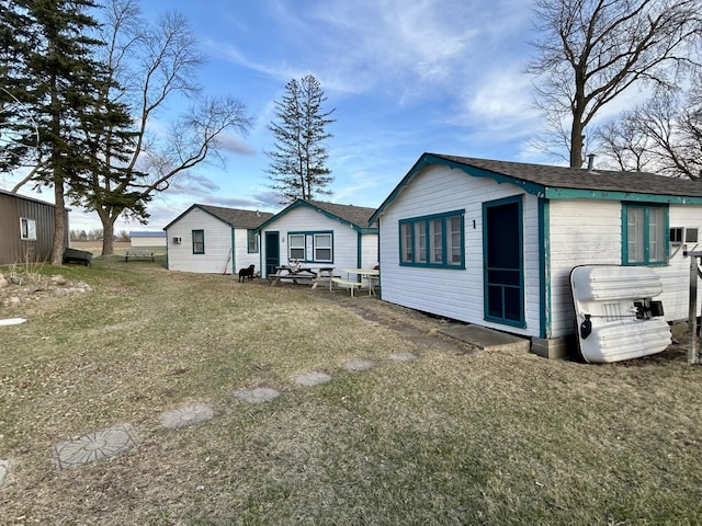 back of property with an outbuilding, roof with shingles, and a yard