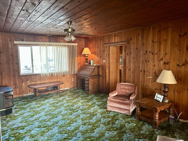 sitting room with wood ceiling, wooden walls, carpet floors, and a ceiling fan
