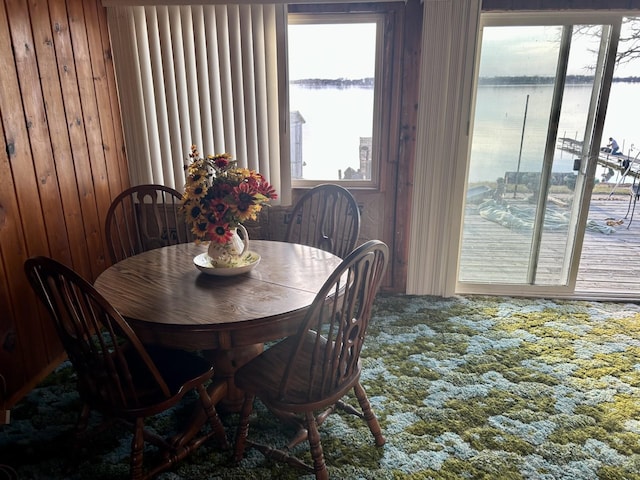 carpeted dining area with wood walls and a water view