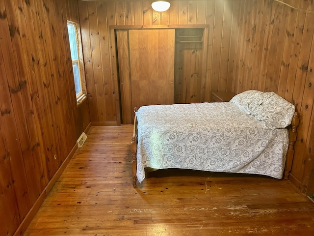 bedroom with a closet, wooden walls, wood-type flooring, baseboards, and visible vents