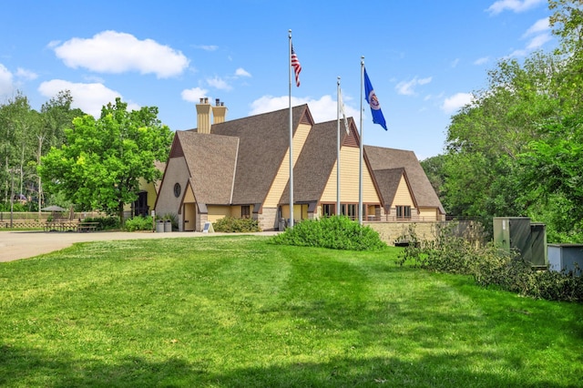 view of front of property with a chimney, a front lawn, roof with shingles, and stone siding