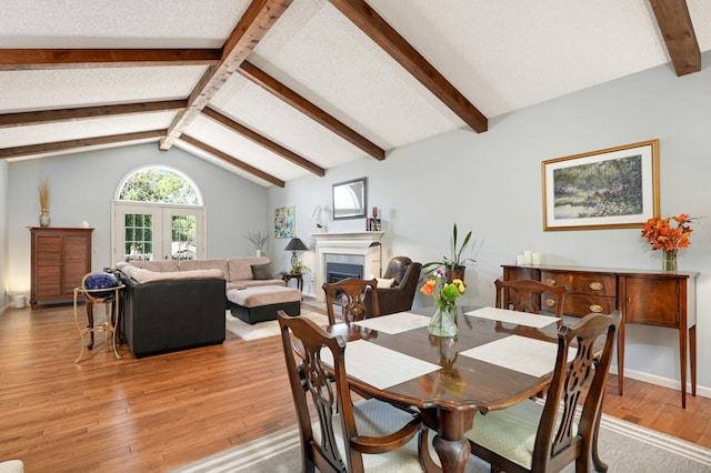 dining area with french doors, a fireplace, baseboards, lofted ceiling with beams, and light wood finished floors