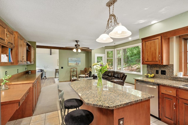 kitchen with a ceiling fan, a kitchen island, stainless steel dishwasher, light stone countertops, and open floor plan