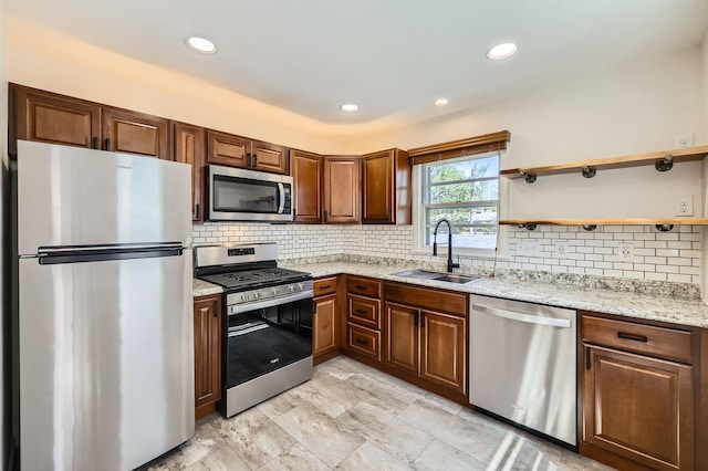 kitchen featuring appliances with stainless steel finishes, decorative backsplash, light stone countertops, and a sink