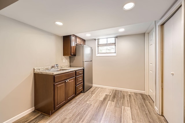 kitchen featuring a sink, freestanding refrigerator, light wood-style flooring, light countertops, and baseboards