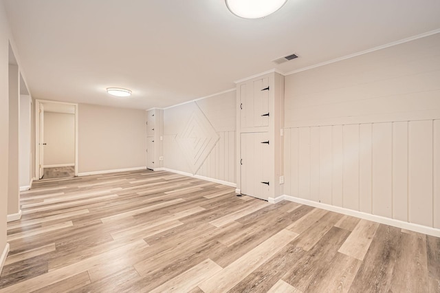 finished basement featuring ornamental molding, a decorative wall, visible vents, and light wood-style floors