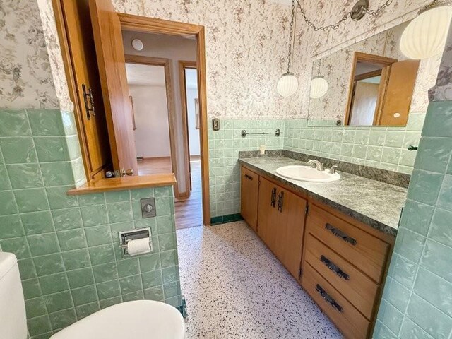 1254 State St, Fairmont, MN 56031 - half bathroom with wallpapered walls, vanity, tile walls, a wainscoted wall, and toilet